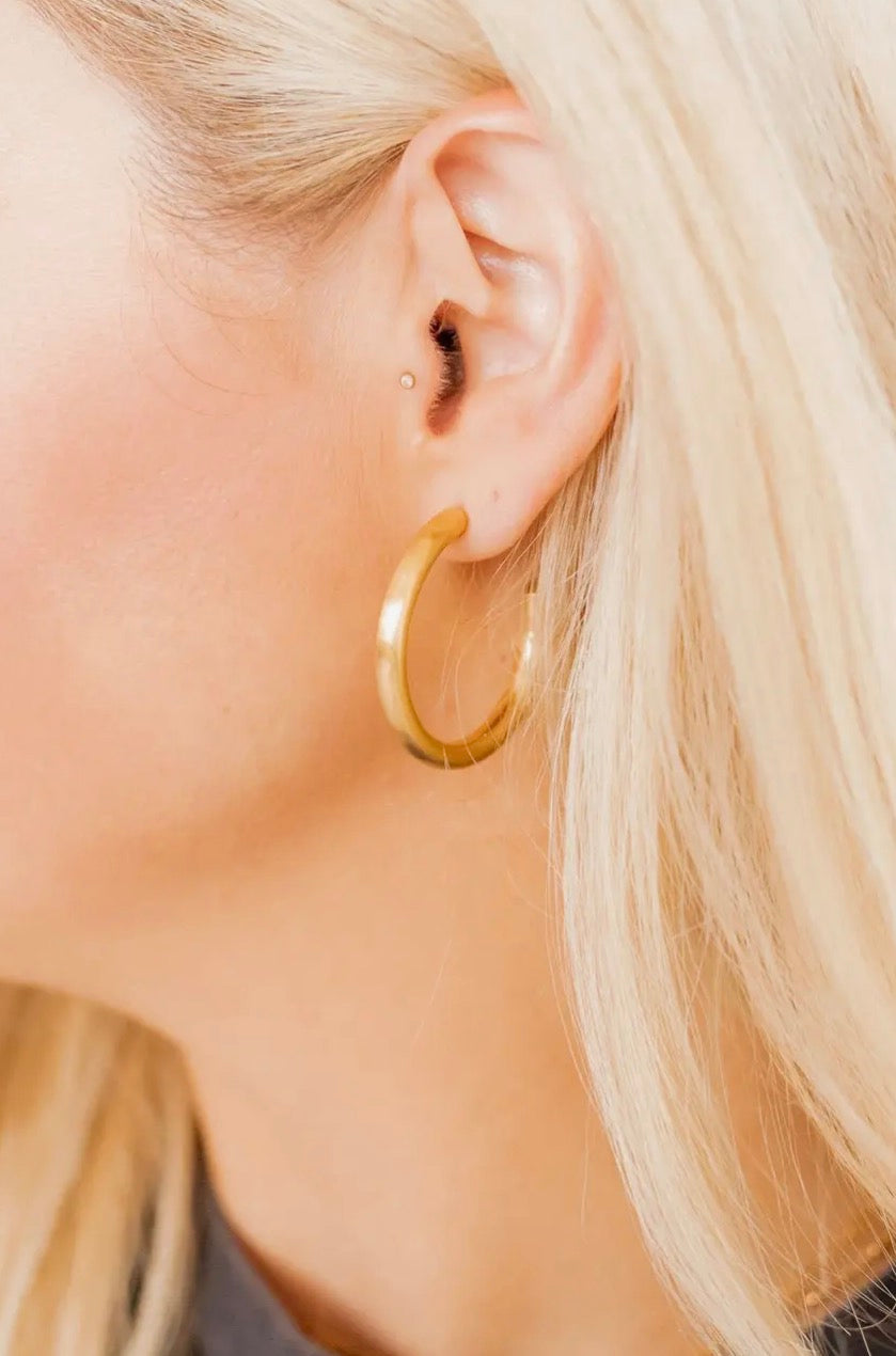 A pair of shiny gold hoop earrings from Linny CO, showcasing their classic circular design and polished finish.