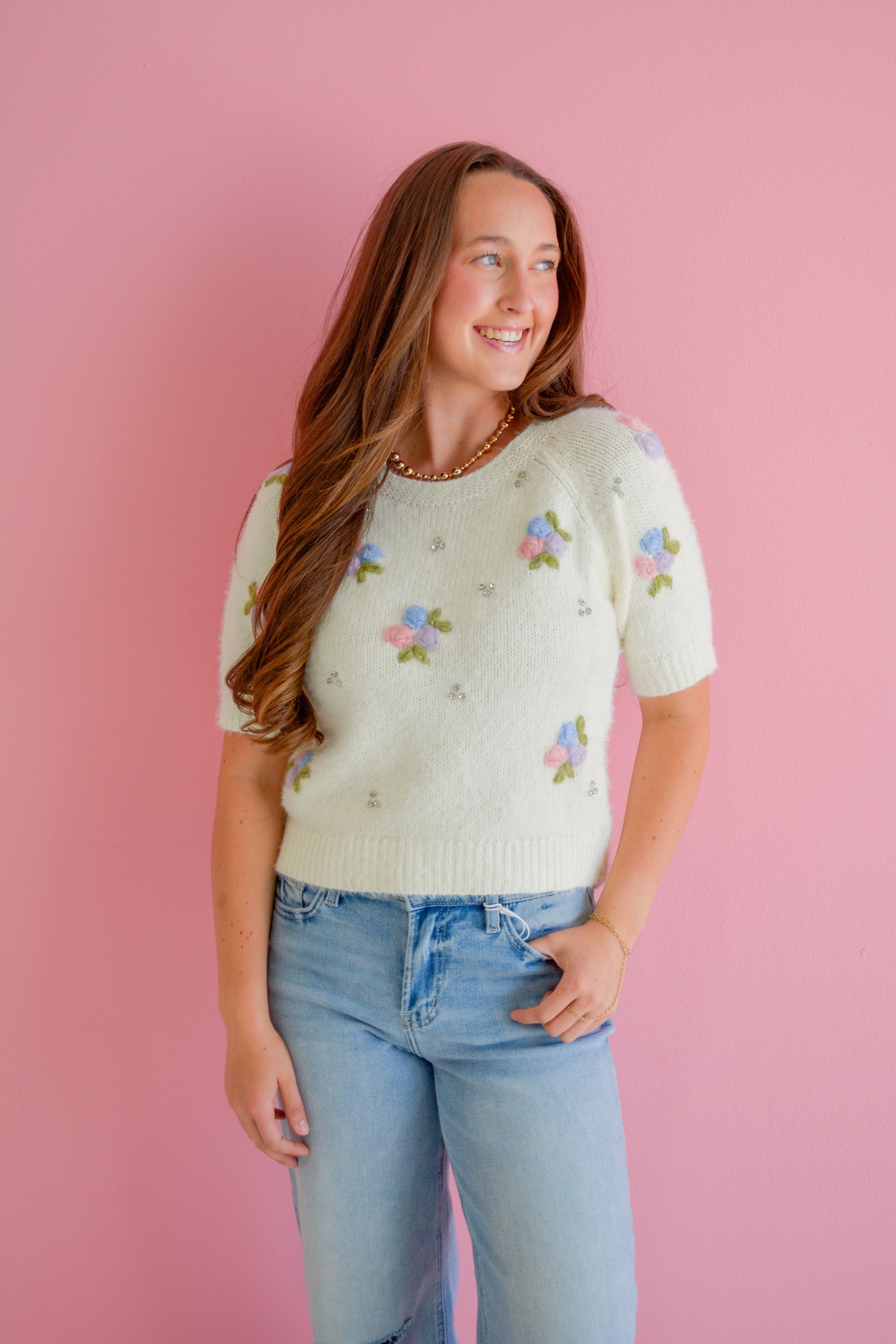 In February Bloom and Sparkle sweater featuring a cozy knit fabric with floral and sparkle embellishments, displayed on a hanger.