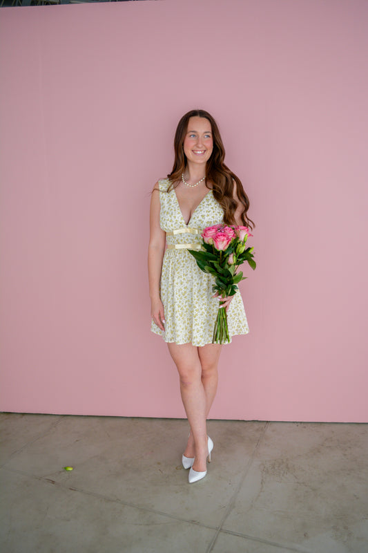 Storia Sunlit Petal Bow Dress for girls, featuring a floral design with a bow detail, displayed on a hanger.