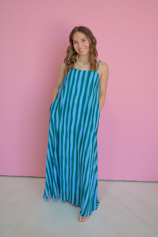 TCEC Island Escape Maxi Dress displayed on a hanger, featuring a flowing fabric, tropical print, and sleeveless design for warm weather.
